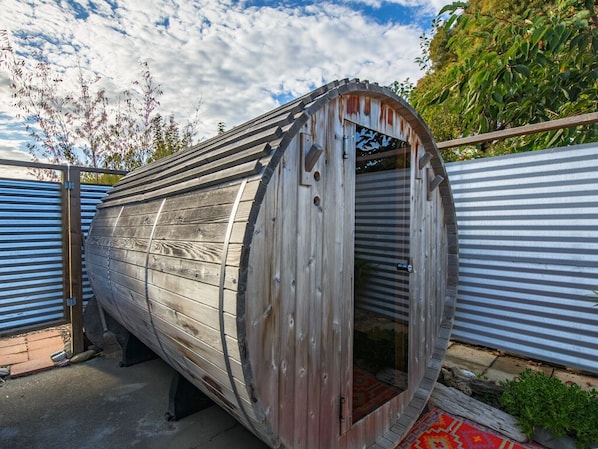 A cylindrical wooden structure with a door, possibly a sauna or a similar facility, surrounded by metal fencing.