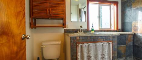 A bathroom with a toilet, a wooden cabinet, a sink with a mirror, and a shower area.