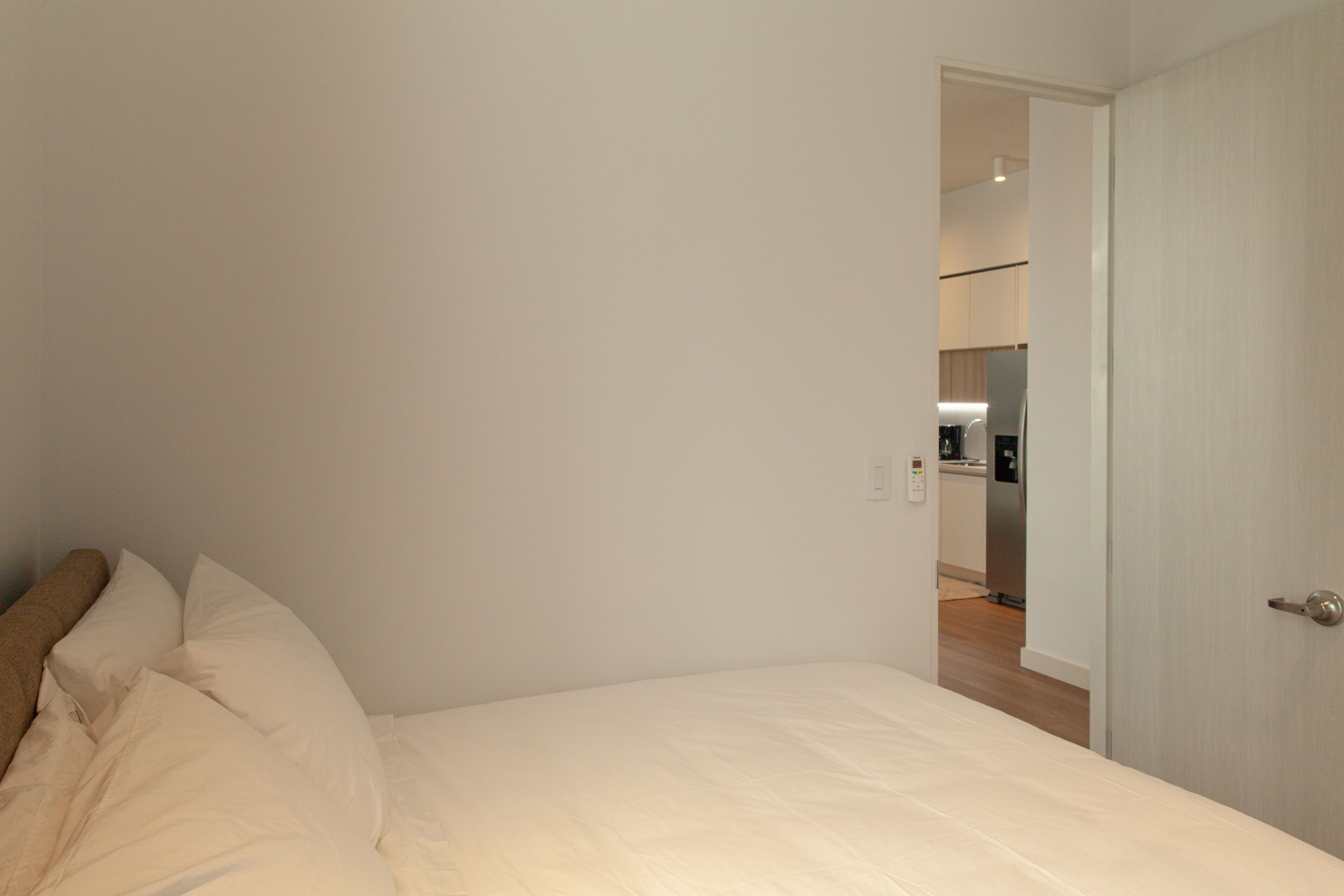 Ein Schlafzimmer mit einem Bett, einer zur Küche führenden Tür und einer weißen Wand.