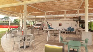 Un cafè a l'aire lliure amb taules i cadires, un mural de un pavó i un camió de menjar.