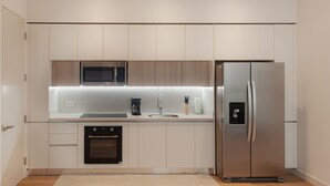 Una cuina moderna amb armaris blancs, un forn de microones integrat, un frigorífic d'acer inoxidable, una cafetera i un rentaplats.