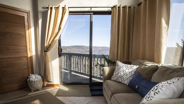Un balcon avec vue sur les collines, une porte-fenêtre coulissante, un canapé avec des coussins à motifs et un panier en osier.