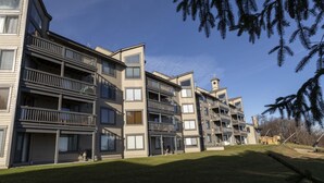 Un immeuble résidentiel à plusieurs étages, doté de balcons, d’une petite structure ressemblant à une tour et d’un espace verdoyant à l’avant.