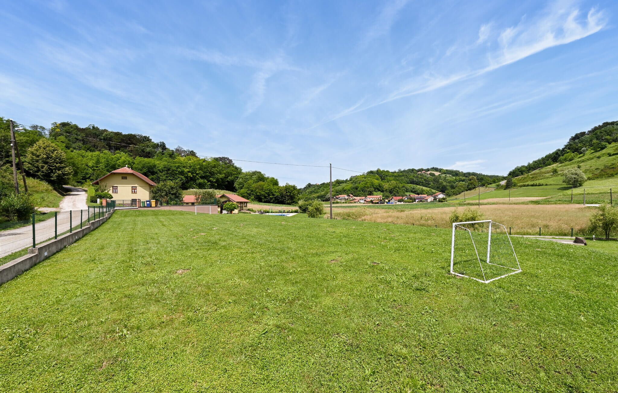 Un champ herbeux avec un but de football, un bâtiment jaune et des maisons en arrière-plan.