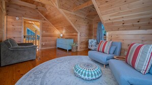 L’intérieur d’une cabane en rondins, avec une chambre à coucher située en mezzanine, un canapé gris, un canapé bleu et un tapis rond.