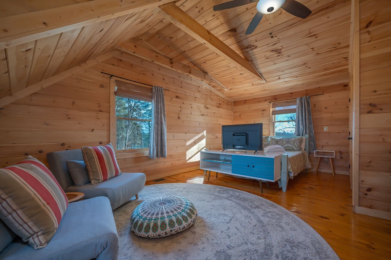 L’intérieur d’un chalet accueillant, avec un plafond en bois, un canapé agrémenté de coussins à rayures, un téléviseur et un lit avec une commode bleue.