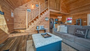 L’intérieur d’un chalet en bois comprend un escalier, un canapé, une table basse et un coin cuisine.