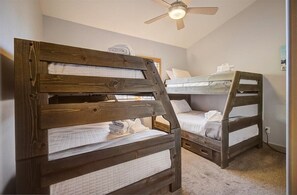 A room with two bunk beds made of wood, a ceiling fan, and a light fixture.
