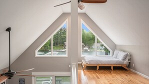 Un dormitorio con techo inclinado, ventanas amplias, cama de madera y ventilador de techo.