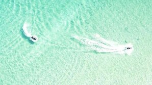 Una vista despejada de una playa con dos barcos creando ondas en el agua.
