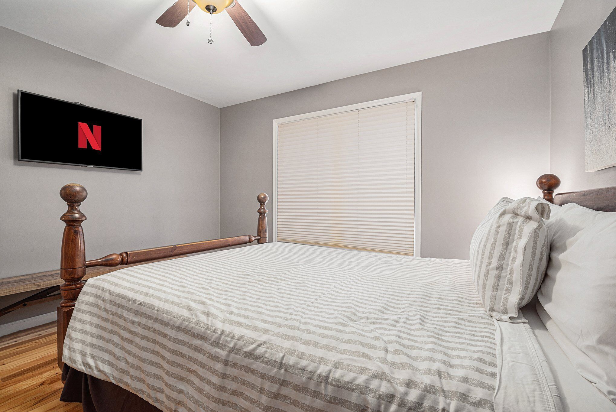 A bedroom with a bed, a TV mounted on the wall, and a ceiling fan.