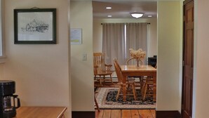 Un corridoio che conduce a una sala da pranzo con un tavolo e sedie di legno, una macchina da caffè su un bancone e un quadro appeso al muro.