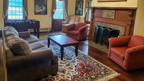 Un salón con una mesa de fútbol, dos sillones, un sofá, una chimenea y una araña.
