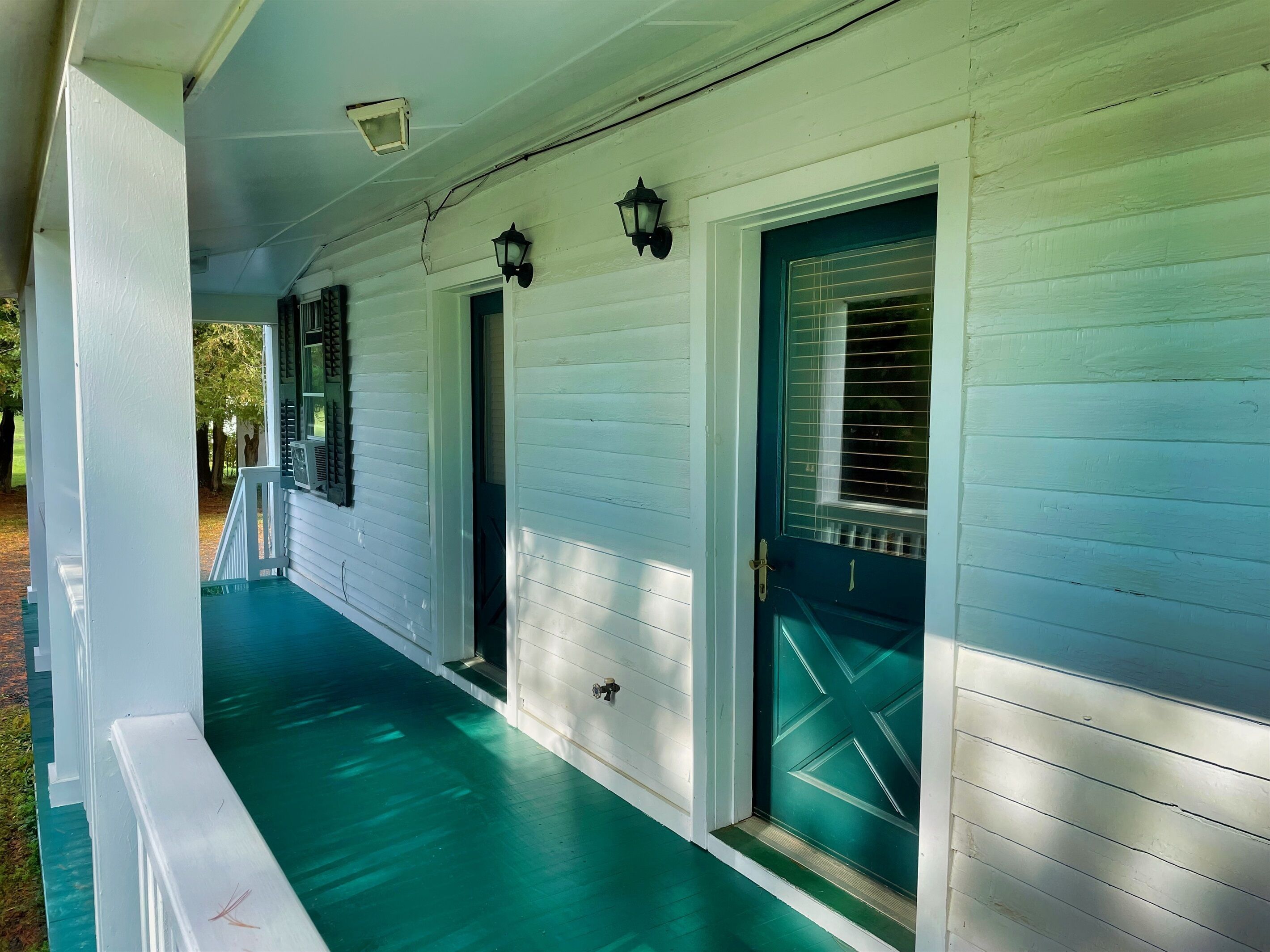 A porch with white siding and a green floor, two doors with windows, and two wall-mounted lanterns.