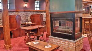 Un restaurante con muebles de madera, chimenea de ladrillo y alfombra roja con estampado.