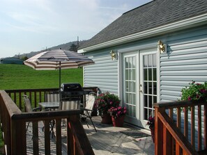 A deck with a grill, chairs, and an umbrella. - Breezy Meadow One Custom-built cottage, 1 of 2, under 1 mile from Dreams Park (Milford)
