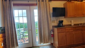 A kitchen with wooden cabinets, a television mounted above the counter, and a sliding glass door leading to an outdoor patio. - Breezy Meadow Two 2 of 2,custom built cottage, under a mile from CDP (Milford)