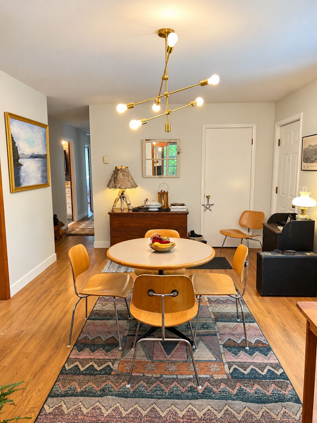 A dining area with a round table, chairs, a chandelier, a mirror, and a door.