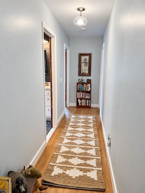 A hallway with a patterned rug, a bookshelf, and a ceiling light fixture. - Comfortable Country Charm with Otsego Lake Access (Cooperstown)