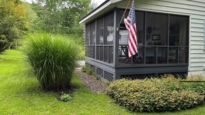Een huis met een veranda, een grote Amerikaanse vlag en een tuin met diverse planten.