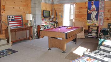 A room with a pool table, a television, and a bookshelf.
