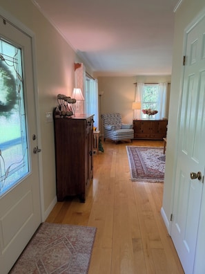 A hallway with wooden flooring, a dark wooden cabinet, a plaid armchair, and a patterned rug. - Changing Seasons - Game room, immaculate ranch (Hartwick)