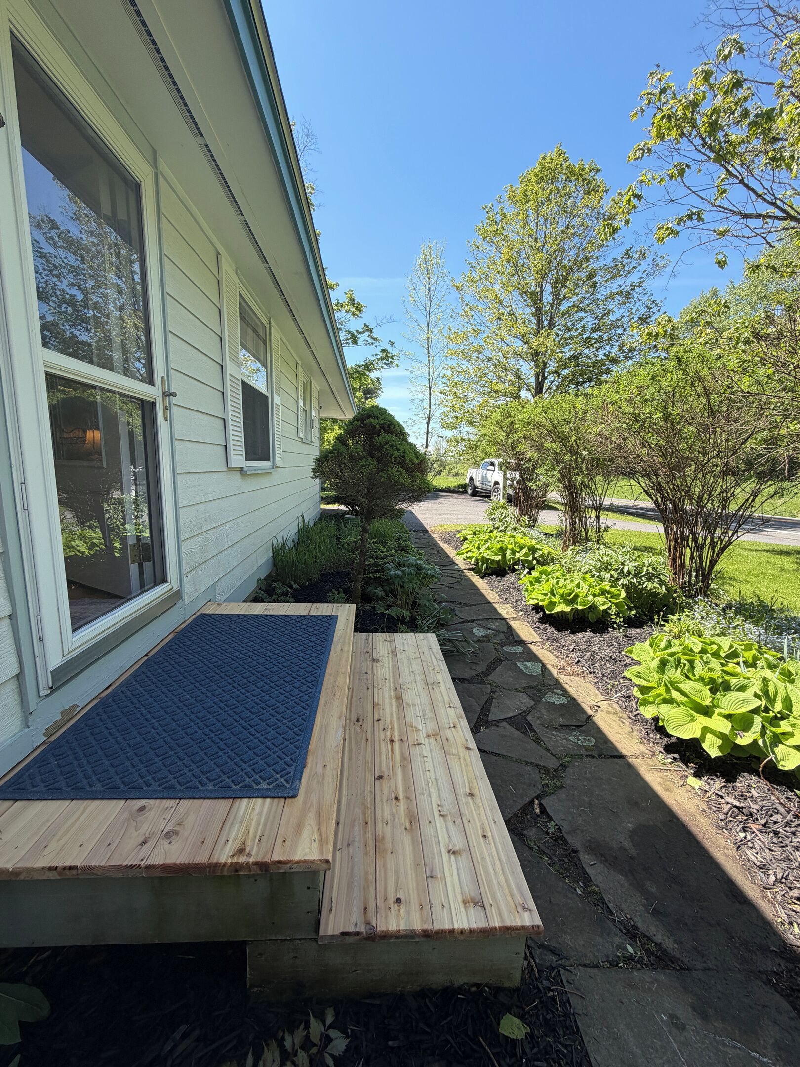 A house with a wooden deck, a stone pathway, and a variety of plants.