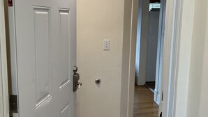A hallway with a white door, a light switch, and a wooden floor. - City Fox 1, 1 of 4, recent renovation in Oneonta, Convenient to All Star Village (Oneonta)