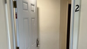 Een gang met een witte deur, een houten vloer en het nummer '2' op de muur.
