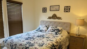 Een slaapkamer met een bloemenbedekking, een gestapeld hoofdbord, een bedlampje en decoratieve muurkunst.