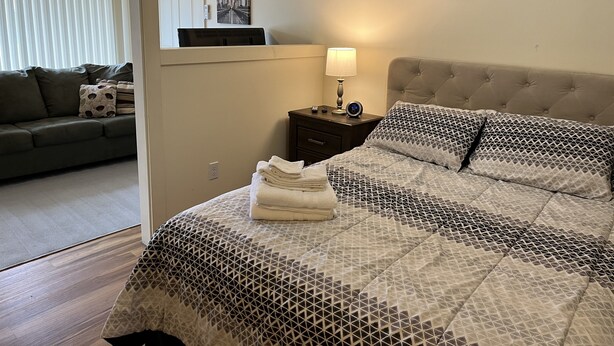 Une chambre à coucher bien rangée, avec un lit, une table de chevet, une lampe, une horloge murale et une fenêtre.
