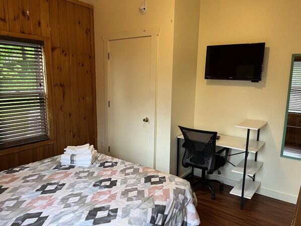Une chambre à coucher avec un lit, un bureau, une chaise, une télévision et une porte.
