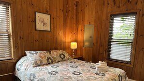 Dormitorio con paneles de madera, una cama, una mesita de noche, una lámpara y un cuadro enmarcado en la pared.