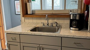 A kitchen with a double sink, wooden window frame, and a coffee maker on the counter. - Clinton House, Charming Cape Cod home decorated with flair in downtown Oneonta (Oneonta)