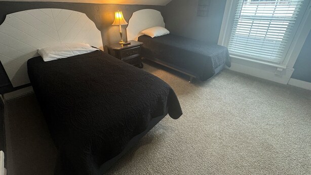 A bedroom with two beds, a nightstand with a lamp, and a window with blinds.