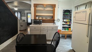 A compact kitchen with a microwave, a wooden shelf, and a refrigerator. - Clinton House, Charming Cape Cod home decorated with flair in downtown Oneonta (Oneonta)