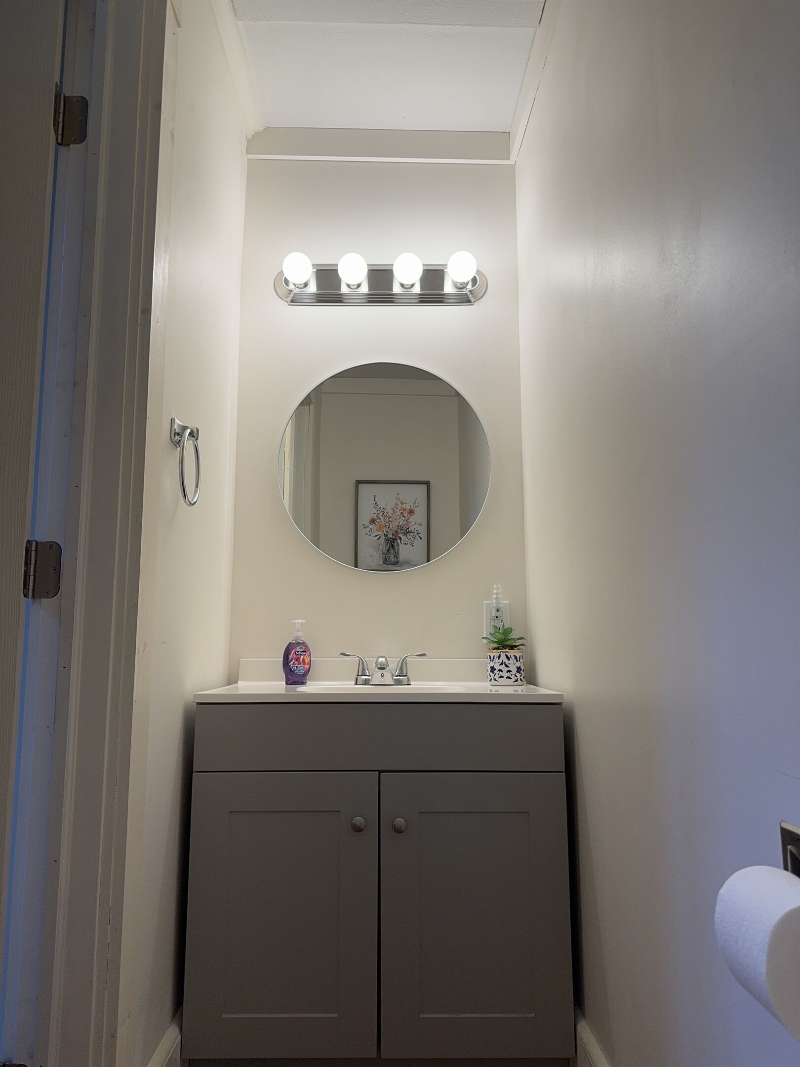 A bathroom with a vanity, a round mirror, and a lighted vanity mirror.