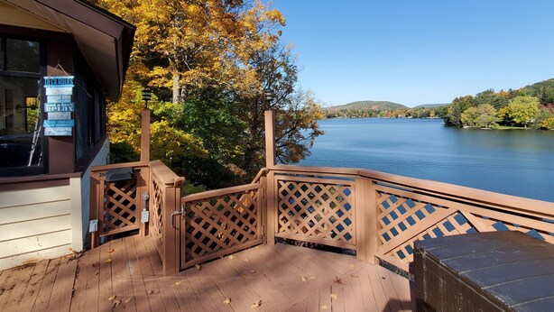 A wooden deck with a lattice railing overlooking a lake, a sign with rules, and autumn foliage. - Colone Cottage, Goodyear Lake, swimming, fishing, 3 kayaks, captivating view (Oneonta)