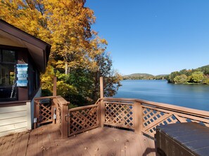 A wooden deck with a lattice railing overlooking a lake, a sign with rules, and autumn foliage. - Colone Cottage, Goodyear Lake, swimming, fishing, 3 kayaks, captivating view (Oneonta)