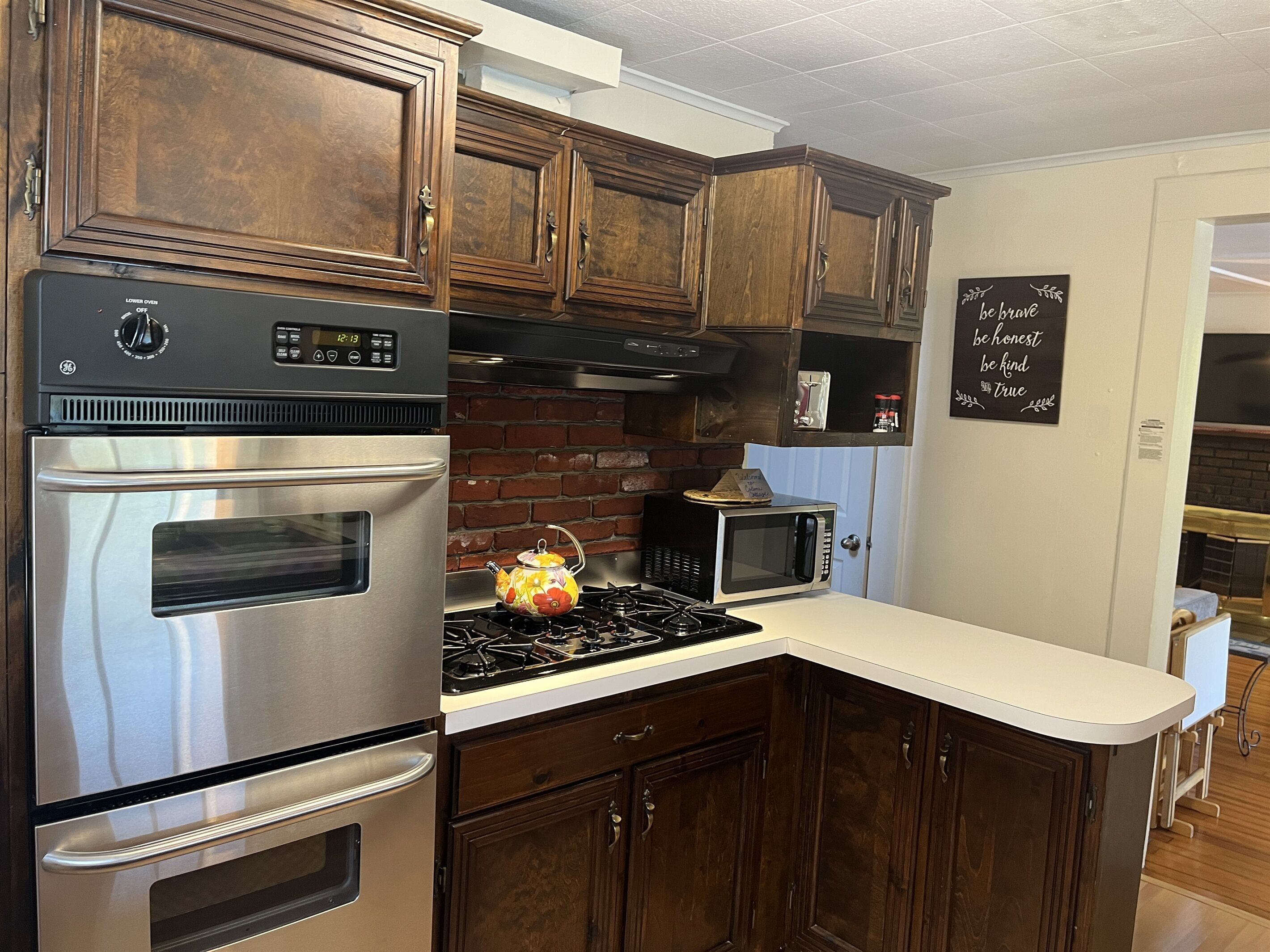 A kitchen with dark wooden cabinets, stainless steel appliances, a brick backsplash, and a chalkboard with motivational quotes.