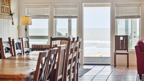 Un comedor con una mesa y sillas de madera, una lámpara y vista al océano a través de amplios ventanales.