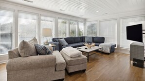 A modern living room with a sectional sofa, ottoman, coffee table, and a flat-screen TV. - Across street from beach, Renovated, Wild Dunes - 7 Fairway Oaks (Isle Of Palms)
