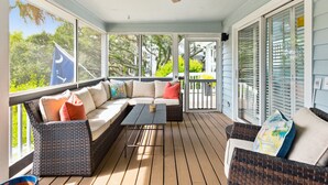 A covered outdoor seating area with wicker furniture, a ceiling fan, and large windows offering views of greenery. - Across street from beach, Renovated, Wild Dunes - 7 Fairway Oaks (Isle Of Palms)