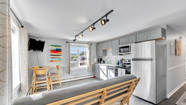 A modern kitchen with a built-in oven, microwave, and refrigerator, a dining area with a table and chairs, and a bench with a cushion. - #1 of 11 Units in Village of Cooperstown Apt Bldg (Cooperstown)