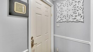 A hallway with a white door, a wall-mounted decorative panel, and a sign indicating the apartment number. - #1 of 11 Units in Village of Cooperstown Apt Bldg (Cooperstown)