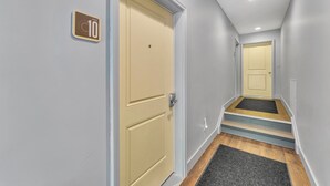Un pasillo estrecho con una puerta color beige marcada con un número, un rellano alfombrado y otra puerta al final.