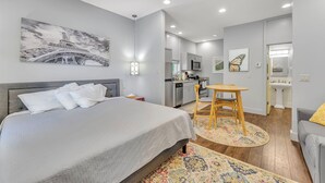 Un dormitorio moderno con una cama, una pequeña mesa de comedor y una kitchenette al fondo.