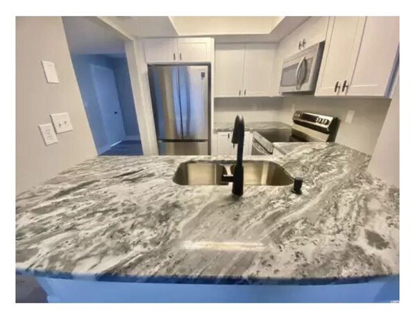 A kitchen with a marble countertop, stainless steel sink, and white cabinets. - Relax in our quiet community surrounded by nature , golf courses & Apache pier (Myrtle Beach)