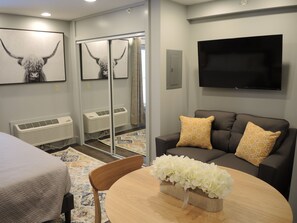Una habitación de hotel moderna con sofá, televisión, cama y obras de arte en las paredes.
