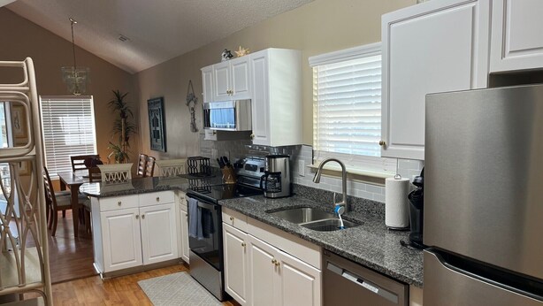 A kitchen with white cabinets, a stainless steel refrigerator, a microwave, and a sink.